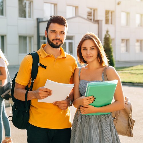 Zwei Studenten vor einem Universitätsgebäude halten Studienunterlagen einer technischen Universität in Österreich im Arm.