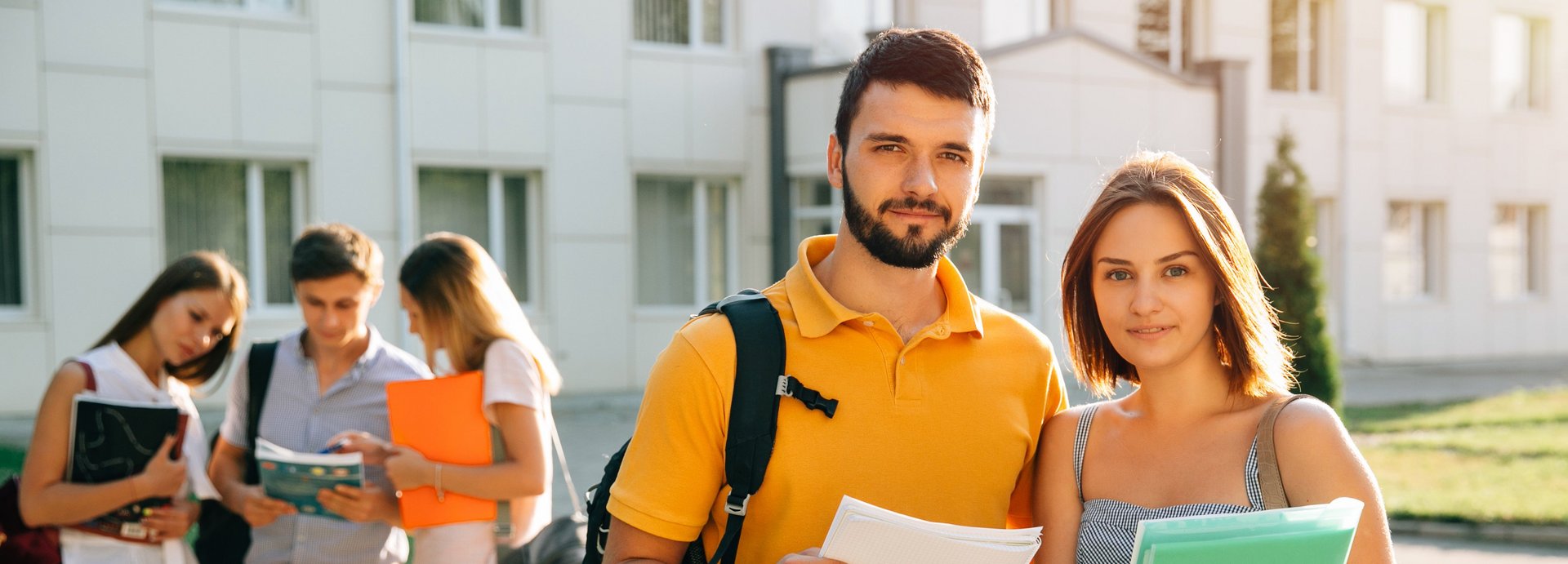 Zwei Studenten vor einem Universitätsgebäude halten Studienunterlagen einer technischen Universität in Österreich im Arm.