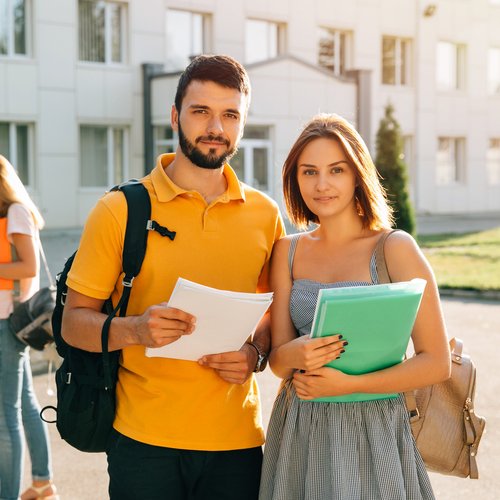 Two students in front of a university building holding study documents from a technical university in Austria.