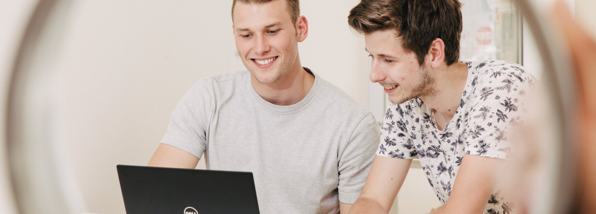 Studierende sitzen vor dem Laptop und lächeln