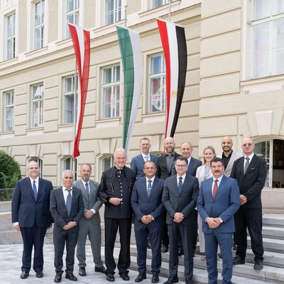 Gruppenfoto von Vertreterinnen und Vertretern zweier Institutionen vor einem historischen Gebäude mit drei vertikal gehissten Fahnen, u. a. Österreich und Ägypten.