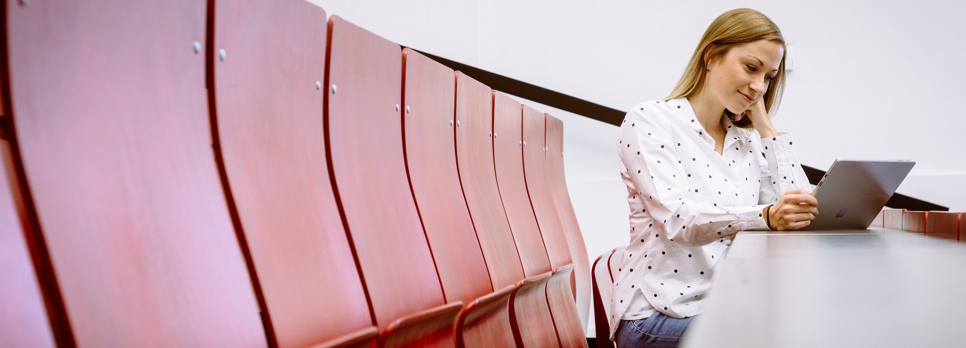 Eine Studentin sitzt im Hörsaal und sieht auf einen Laptop.