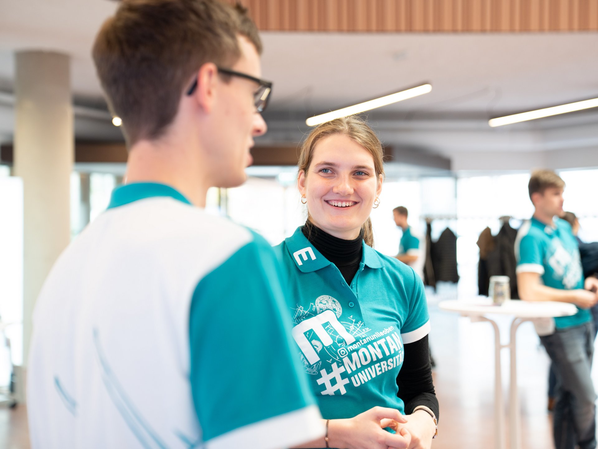 Eine junge Frau und ein junger Mann stehen zusammen und sie lächelt.