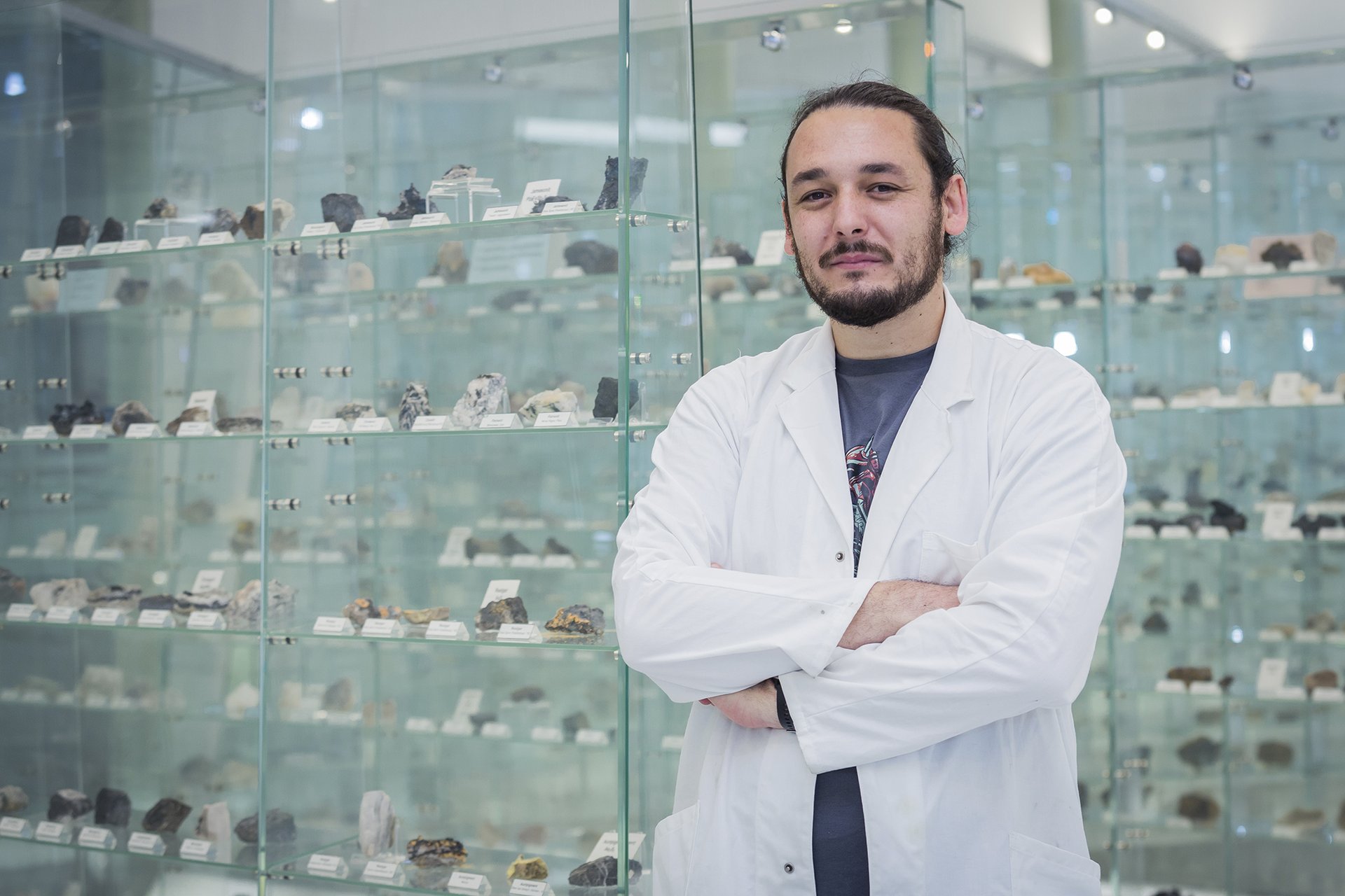 Mann im weißen Laborkittel vor Vitrine mit Gesteinen.