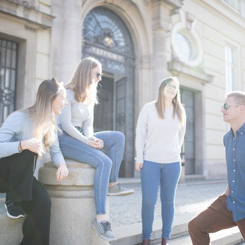 Studierende stehen an den Treppen am Eingang des Hauptgebäudes und unterhalten sich