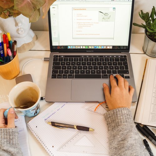 Frauenhände mit Kaffeetasse vor einem Laptopbildschirm.