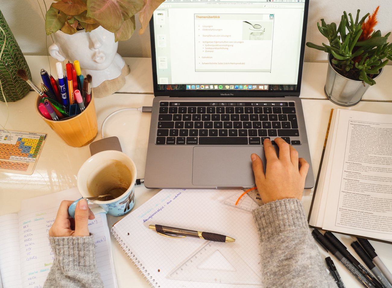 Frauenhände mit Kaffeetasse vor einem Laptopbildschirm.