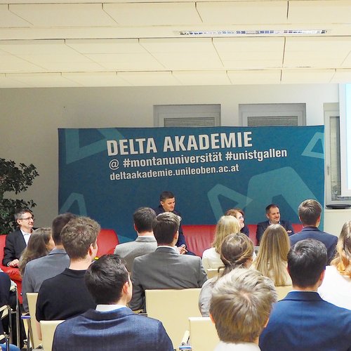 Lecturer in front of students and a poster of the Delta Academy in the background.